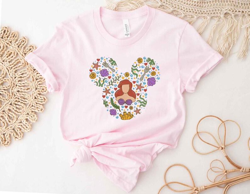 Puede incluir: Camiseta rosa con una silueta de Mickey Mouse compuesta por varias im&aacute;genes de La Sirenita, incluyendo a Ariel, conchas marinas y un tenedor.