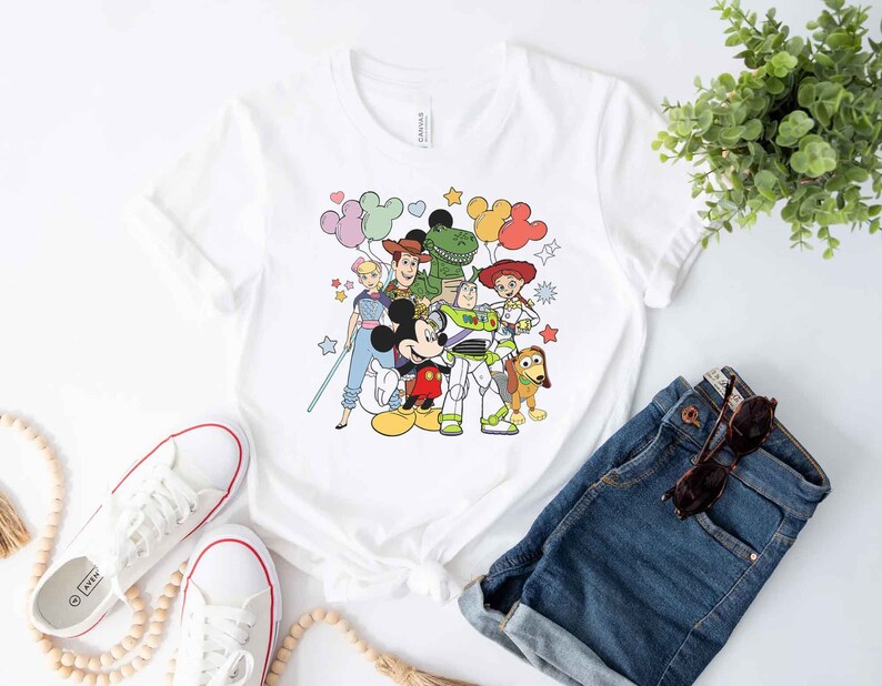 Puede incluir: Camiseta blanca con un gr&aacute;fico colorido de Mickey Mouse, Woody, Buzz Lightyear, Jessie, Rex y algunos globos. El gr&aacute;fico es de estilo de dibujos animados.