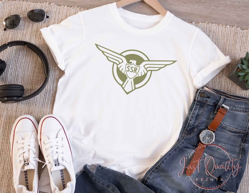 Op de afbeelding: Wit T-shirt met een groene adelaar afbeelding en de tekst "SSR" in een cirkel.