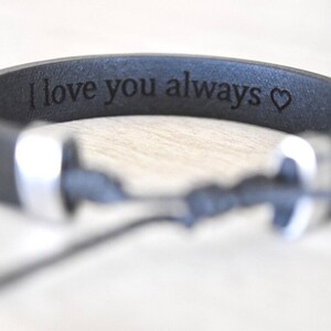 May include: Black leather bracelet with a silver clasp and the inscription "I love you always" with a heart symbol.