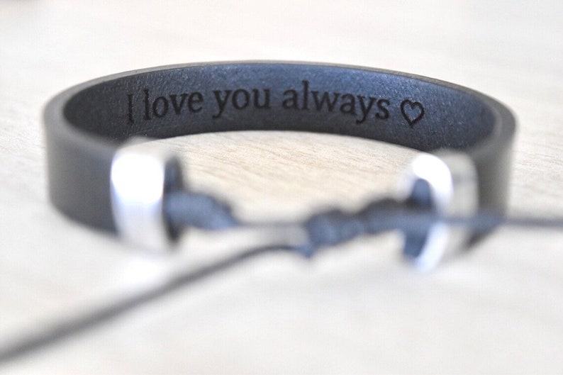 May include: Black leather bracelet with a silver clasp and the inscription "I love you always" with a heart symbol.