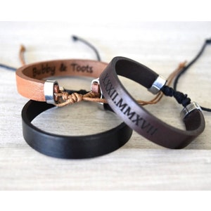 May include: Three leather bracelets with silver clasps. One brown bracelet is engraved with the Roman numerals "XXII.I.MMXVII". One tan bracelet is engraved with the text "Bubbly & Toots". The third bracelet is black.