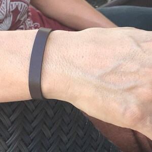 May include: A simple brown leather bracelet on a person's wrist.