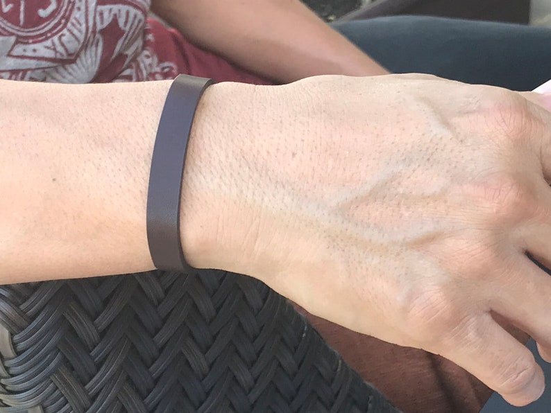May include: A simple brown leather bracelet on a person's wrist.