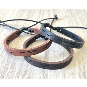 May include: Three leather bracelets with adjustable closures. Each bracelet features a different message in braille, including "You Can Do It" and "With You".