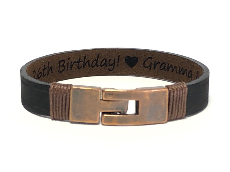 May include: Black leather bracelet with a copper clasp and an engraved message that reads "16th Birthday! &hearts; Grandma".