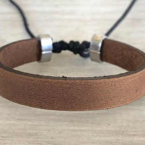 May include: A brown leather bracelet with silver metal clasps and a black cord.