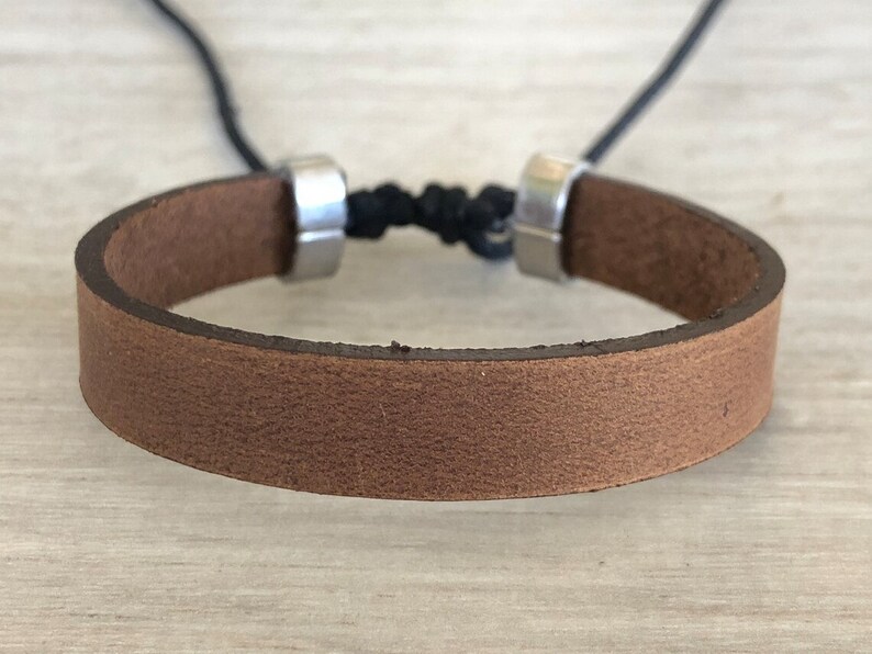 May include: A brown leather bracelet with silver metal clasps and a black cord.