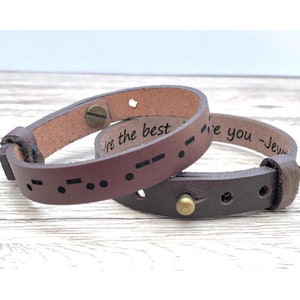 Puede incluir: Dos pulseras de cuero marrón con texto grabado. Una pulsera dice "Te amo" y la otra "Eres el mejor".