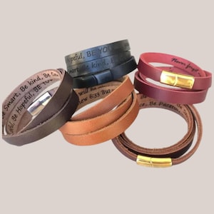 Może przedstawiać: Kolekcja skórzanych bransoletek w różnych kolorach, w tym brązowym, czarnym, bordowym i beżowym. Każda bransoletka posiada magnetyczne zapięcie i wygrawerowany inspirujący tekst. Bransoletki są zaprojektowane tak, aby owijać się wokół nadgarstka kilka razy.