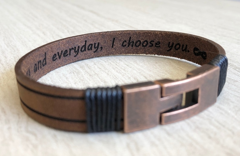 May include: Brown leather bracelet with black braided accents and a copper clasp. The bracelet has the inscription "And everyday, I choose you."