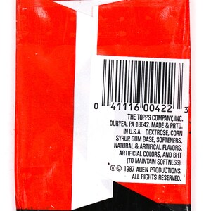 May include: A red and white package with a barcode and text that reads "THE TOPPS COMPANY, INC. DURYEA, PA 18642. MADE & PRTD. IN U.S.A. DEXTROSE, CORN SYRUP, GUM BASE, SOFTENERS, NATURAL & ARTIFICAL FLAVORS, ARTIFICIAL COLORS, AND BHT (TO MAINTAIN SOFTNESS). &copy; 1987 ALIEN PRODUCTIONS. ALL RIGHTS RESERVED."