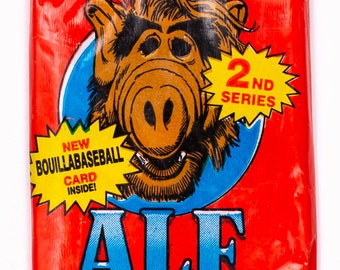 May include: A red and blue trading card pack featuring ALF, a fictional alien character from the 1980s television series. The pack is labeled "2nd Series" and includes 5 cards, 1 sticker, and 1 stick of bubble gum.