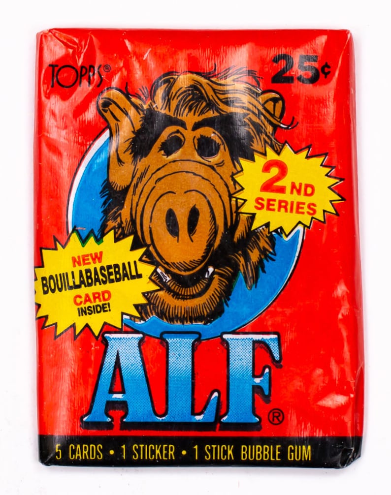 May include: A red and blue trading card pack featuring ALF, a fictional alien character from the 1980s television series. The pack is labeled "2nd Series" and includes 5 cards, 1 sticker, and 1 stick of bubble gum.