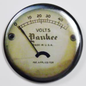 Può includere: Un indicatore rotondo in stile vintage con un ago nero che punta a destra. L'indicatore è etichettato "VOLTS" e "Yankee" con il testo "MADE IN U.S.A." e "PAT. APPLIED FOR".