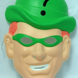 May include: Green plastic mask of the Riddler from Batman. The mask features a green hat with a question mark, green eye mask, and a smiling face.