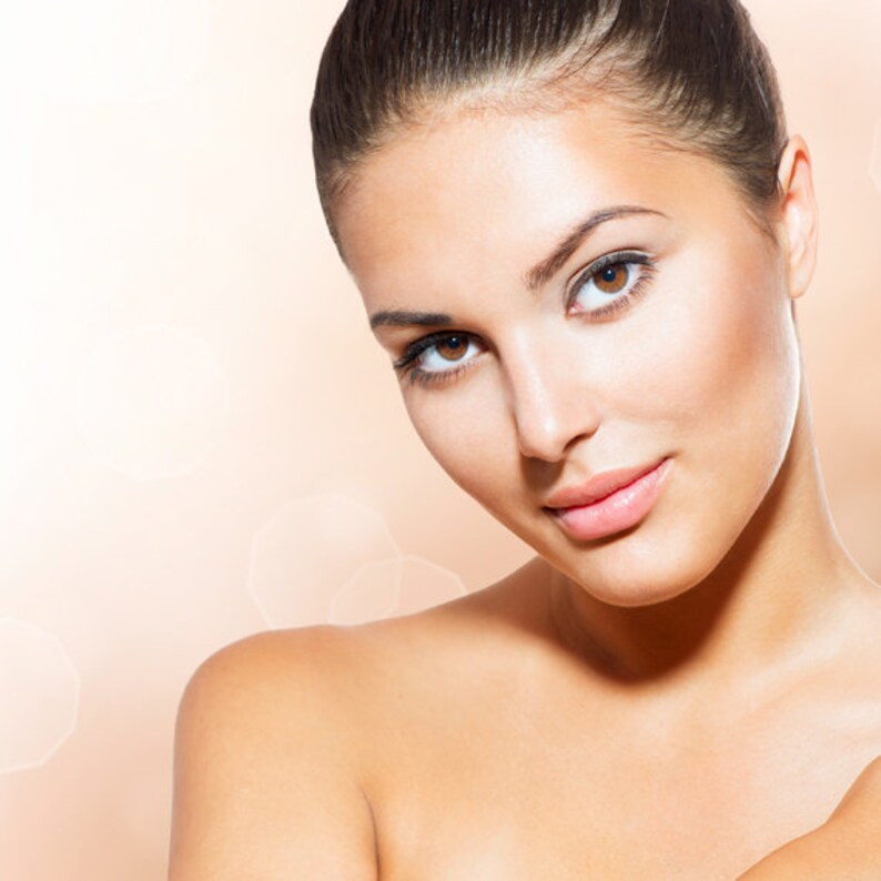 May include: A close-up portrait of a person with brown eyes and dark hair pulled back. The person has a fair complexion and is looking towards the viewer. The background is a soft, blurred peach color with bokeh effects.