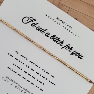 May include: A gold-colored Morse code bracelet with the message "I'd cut a bitch for you" on a white card. The card also displays the Morse code translation and the words "Morse Code Message Bracelet".