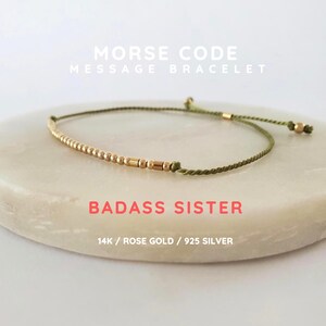 May include: A Morse code message bracelet featuring metallic beads on a thin olive green cord. The text MORSE CODE MESSAGE BRACELET, BADASS SISTER, and 14K / ROSE GOLD / 925 SILVER is printed in white and coral text over the bracelet image.