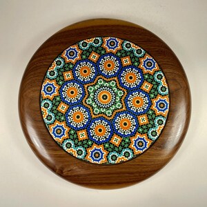 Peut inclure: Plateau rond en bois avec incrustation de carreaux de mosaïque colorés. Le carrelage présente un motif géométrique avec des formes orange, bleues, vertes et blanches. Le plateau a une finition brun foncé et polie.