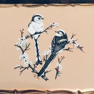 May include: A vintage gold-toned trinket box with a delicate floral design featuring two black and white birds perched on branches with white blossoms. The box has a scalloped edge and is signed "Julia Green".