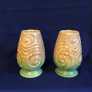 May include: Two green and brown ceramic vases with a swirl design. The vases are approximately 15 cm tall and have a rounded shape.