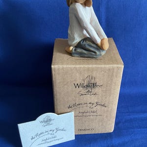 May include: A Willow Tree "Joyful Child" figurine, featuring a seated figure in a white top and gray pants. The figurine is on a brown box with the text "the Roses in my Garden". A small card with the same text is in front.