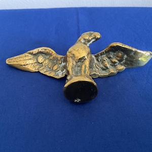 May include: A gold-colored metal eagle figurine with outstretched wings. The eagle is standing on a round base.