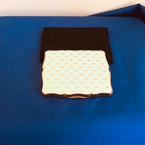 May include: A gold compact with a white and gold crown pattern on the lid. The compact is sitting on a blue surface.