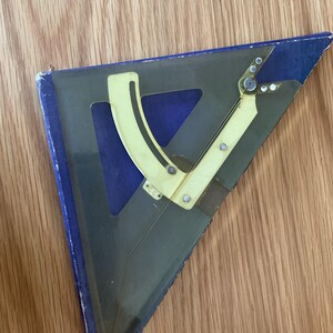 May include: A clear plastic and yellow protractor and triangle ruler set. The set is triangular with a blue backing and yellow adjustable arm. The ruler has a clear plastic body with measurements and markings.