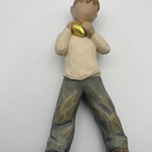 Könnte beinhalten: Eine Holzfigur eines Jungen, der ein goldenes Herz in seinen Händen hält. Der Junge trägt einen weißen Pullover und eine blaue Jeans.