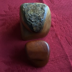 May include: Two wooden sculptures, one is a large, irregularly shaped, dark brown piece with a rough, textured surface. The other is a smaller, smooth, oval-shaped piece, also dark brown.