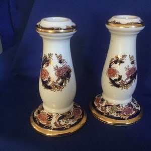 May include: Pair of white ceramic candle holders with blue and gold floral designs.