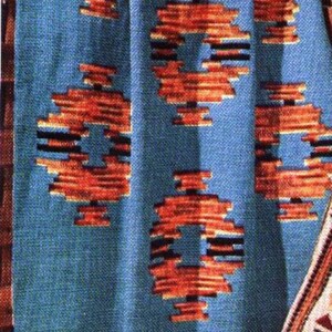 Könnte beinhalten: Blauer gewebter Textil mit einem sich wiederholenden geometrischen Muster in Orange- und Schwarztönen. Der Textil hat einen Fransenrand und ist wahrscheinlich eine Decke oder ein Überwurf.