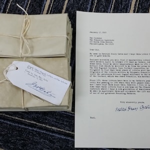 Op de afbeelding: Een stapel bruine papieren enveloppen gebonden met touw en een handgeschreven notitie die luidt "Found 12 Letters Dated 1773 Found by John Allen Gray November 5, 1933". Een brief gedateerd 11 januari 1933, geadresseerd aan de directeur van het Franklin Institute, 20th and the Parkway, Philadelphia, PA 19103, is ook zichtbaar. De brief is ondertekend met "Met vriendelijke groeten,  Peter Henry  Gretz".