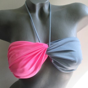 May include: A two-tone bikini top displayed on a mannequin. The top features a halter neck design with a pink fabric on the left side and a gray fabric on the right side. The fabrics are gathered and knotted in the center.