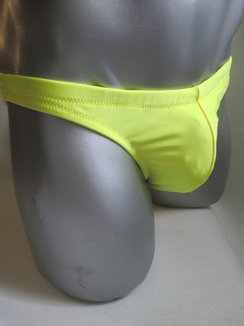 May include: A bright yellow swimsuit with a low rise cut. The swimsuit is made of a smooth, shiny fabric.