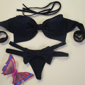 Op de afbeelding: Zwarte bikini top en broek met een strikdetail. De top heeft verstelbare bandjes en de broek heeft een hoge beenuitsnijding.