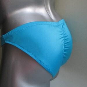 May include: A turquoise blue swimsuit with a low-cut back and a cheeky cut in the front.