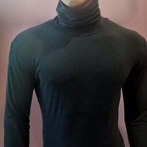 Könnte beinhalten: Ein dunkelgrüner Rollkragen-Body auf einer Schaufensterpuppe. Das langärmlige Kleidungsstück hat einen hohen Ausschnitt und ist figurbetont. Die Schaufensterpuppe hat einen neutralen Gesichtsausdruck und kurzes, helles Haar.