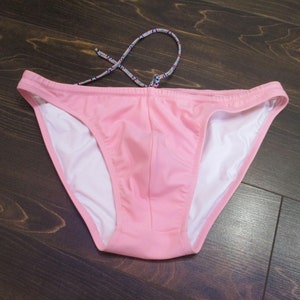 May include: Pink swim briefs with a white lining and a patterned drawstring.