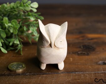 May include: A white wooden owl figurine with large eyes and a simple design. The owl is standing on a wooden surface.