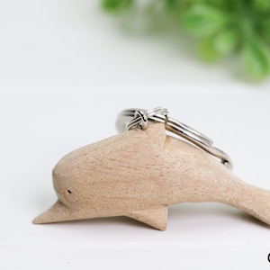 May include: A wooden dolphin keychain with a silver metal key ring. The dolphin is carved in a light brown color and has a smooth finish.