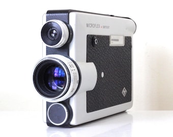May include: A vintage Microflex 8850T camera with a black and white color scheme. The camera features a large lens, a smaller viewfinder, and a textured black panel. The text "MICROFLEX 8850T" is visible on the camera body.