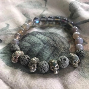 May include: A gray and black beaded bracelet with silver skull charms and lava rock beads.
