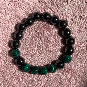 May include: A black and green beaded bracelet with a row of green malachite beads and a row of black hematite beads.