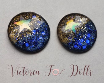 May include: A pair of round resin earrings with a gold and blue glitter background and a holographic star in the center.  The earrings are for dolls.