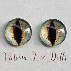 May include: Pair of realistic glass eyes with a green, brown, and black color scheme. The eyes have a cat-like appearance with a vertical pupil.