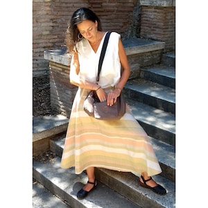 May include: A woman wearing a white sleeveless top and a striped skirt with a brown shoulder bag. She is standing on a set of stone steps.