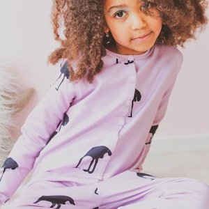 May include: A young girl wearing a lavender long-sleeved pajama onesie with a black flamingo print.